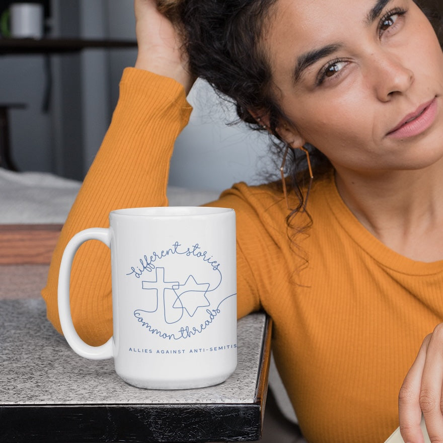 Curly-haired woman looking pensively at the camera with a large ceramic mug on the table in front of her; the mug reads, "Am Yisrael Chai."