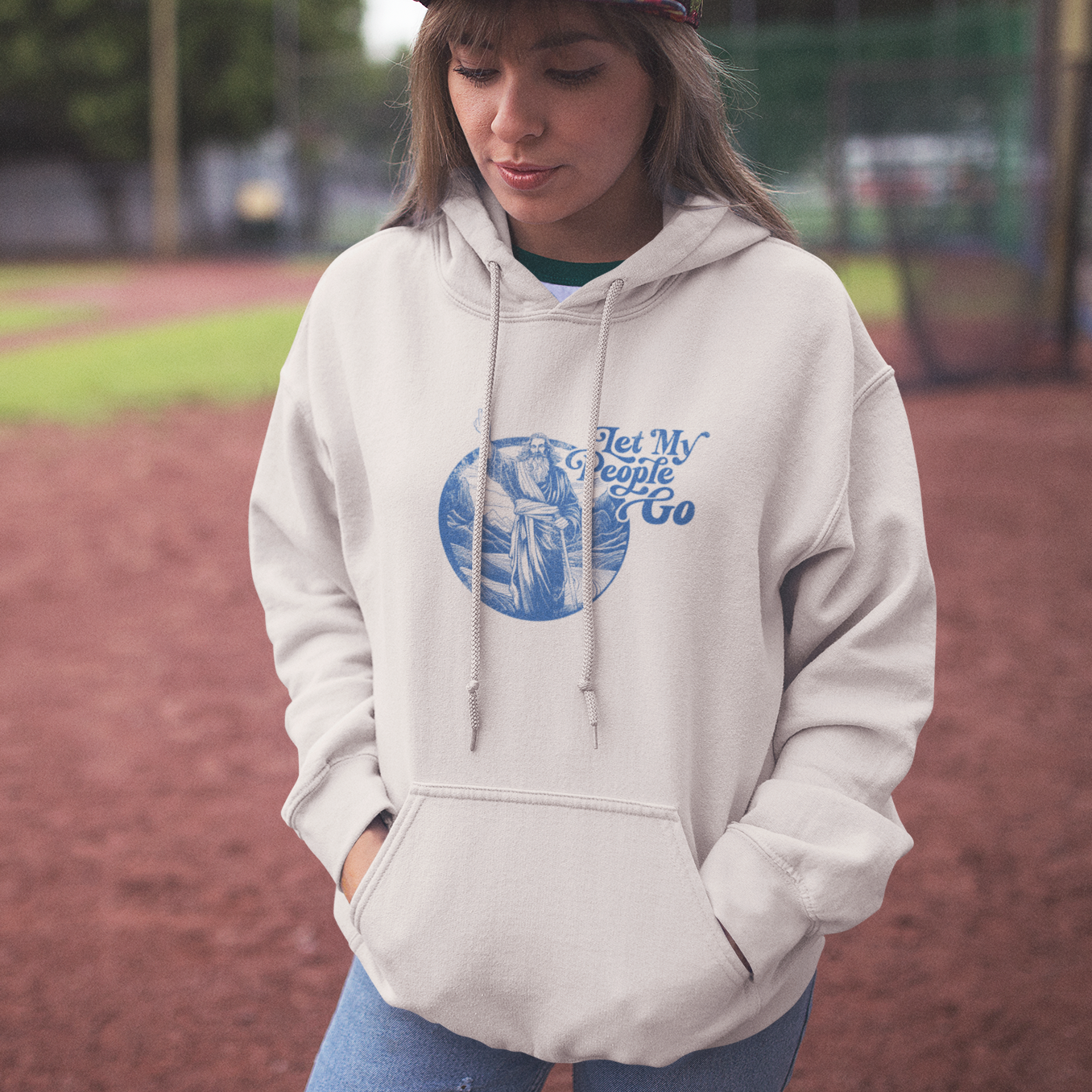 A young woman with curly hair wearing a gray hooded sweatshirt that reads, "Let My People Go" and features an illustration of Moses.