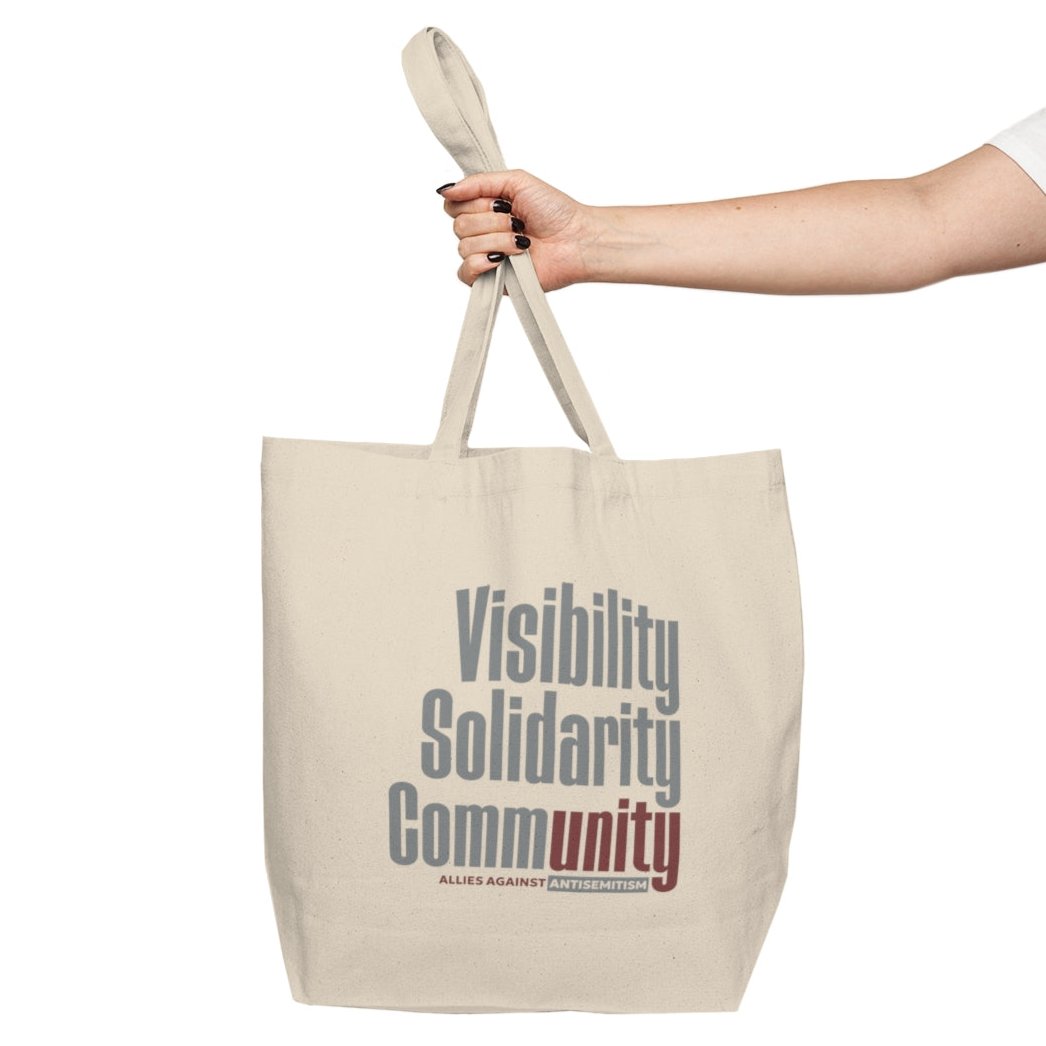 woman's arm and hand holding canvas tote bag with visibility solidarity community in orange, green, and burgundy block letters